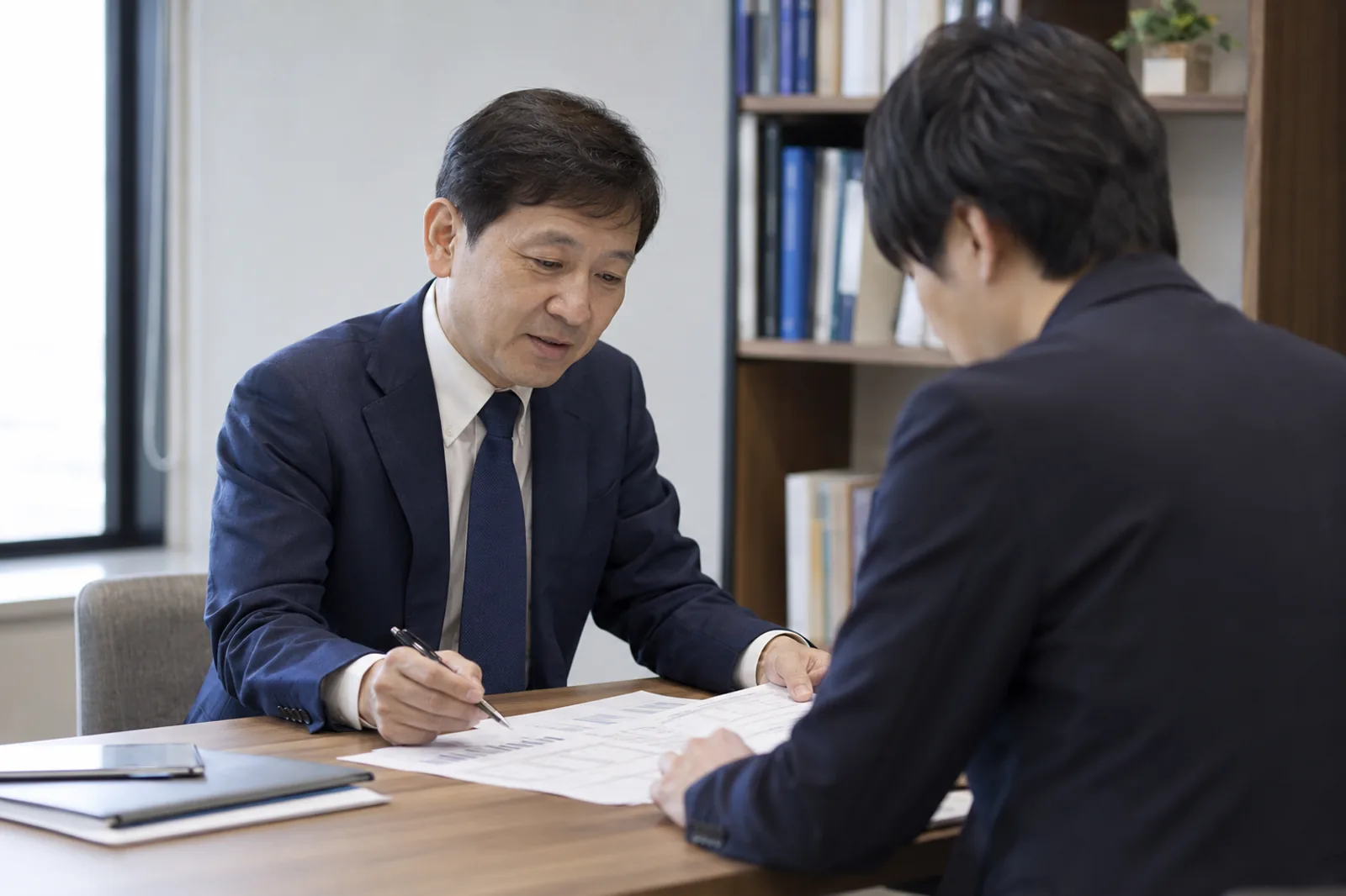 面談テーブルで書類を挟んで話す税理士と相談者