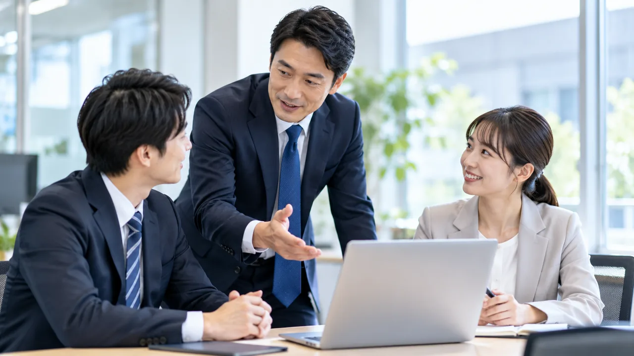 営業所の机で、所長が若手の営業担当2人にノートパソコンを前に指導している様子