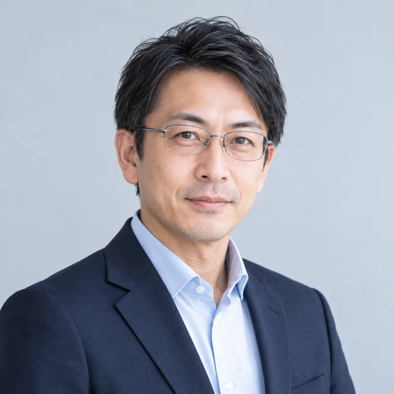 眼鏡をかけ、紺のジャケットに水色のシャツ姿の真柴 健吾