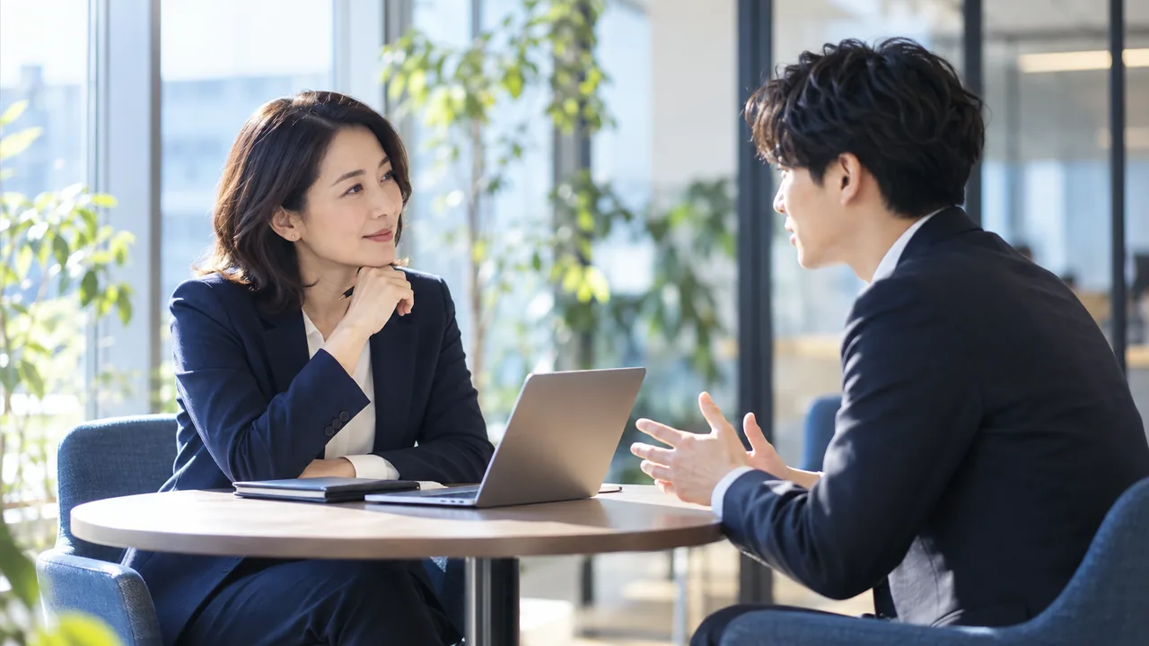 窓際の丸テーブルで、上司と若手社員が一対一で話している様子