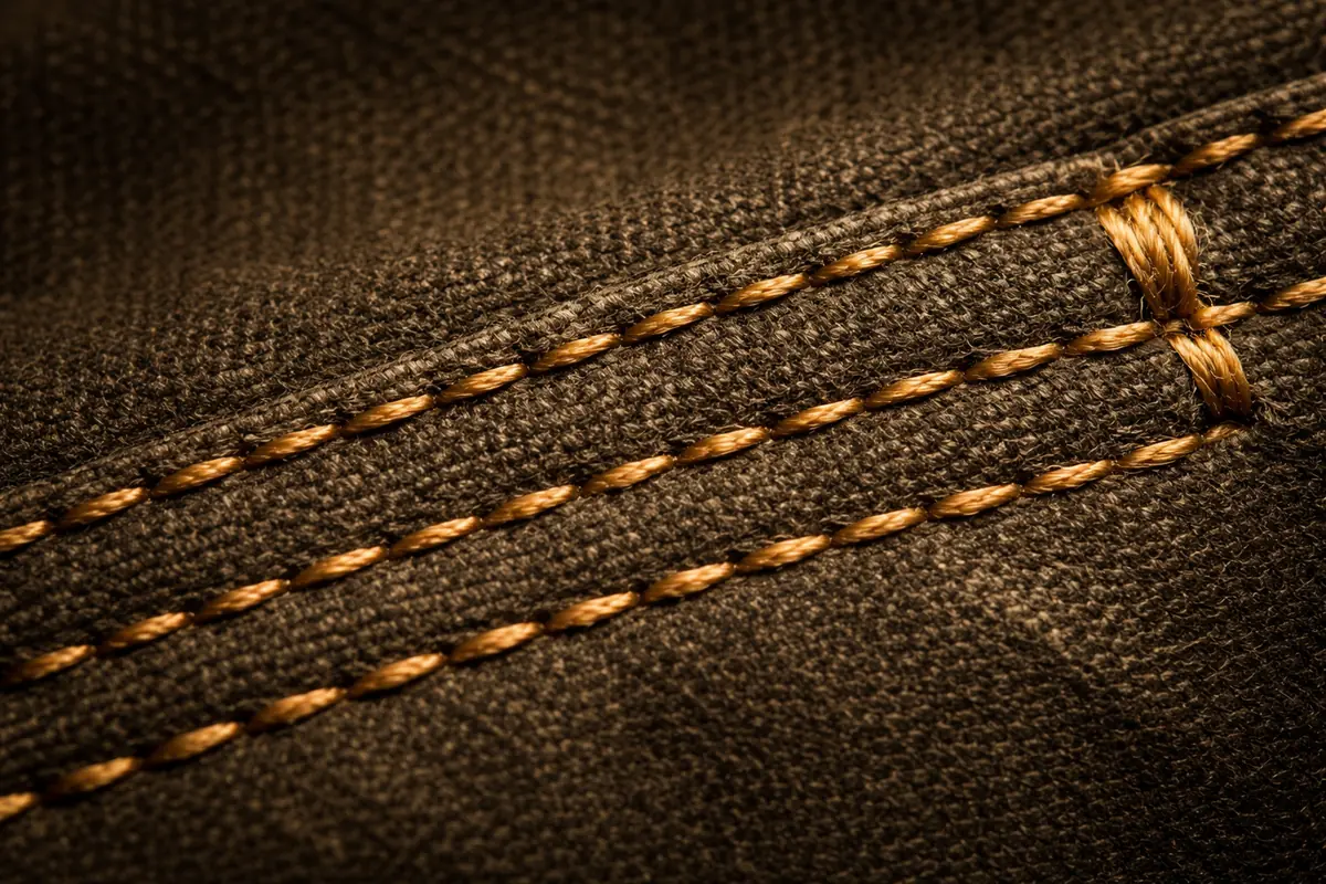 Macro photograph of triple-stitch construction — three parallel rows of golden thread on waxed canvas