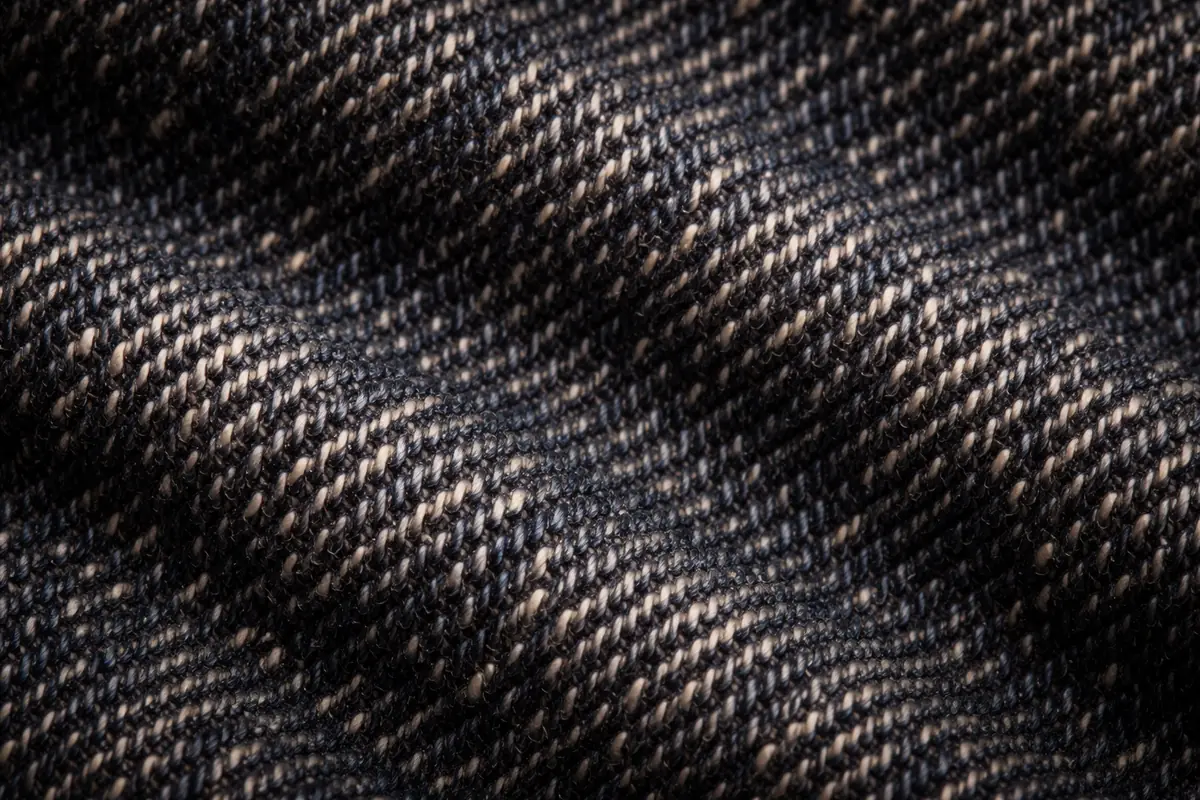 Extreme close-up of raw selvedge denim weave — visible indigo warp and white weft threads, tactile texture